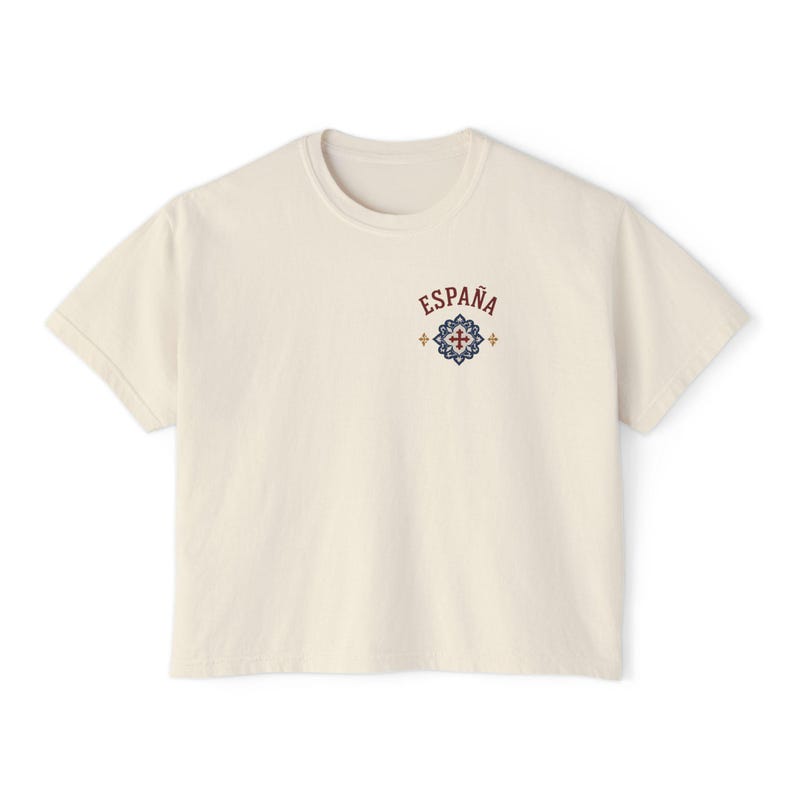 A cream-colored short-sleeved crop top with "ESPAÑA" and a red and blue tile graphic on the left chest, shown flat against a white background.