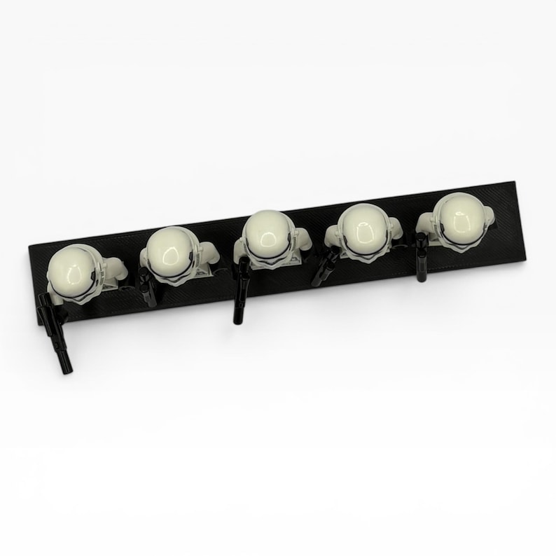May include: Five white plastic stormtrooper minifigures arranged in a row on a rectangular black base. Each figure wears a white helmet and holds a small black blaster accessory. The figures are viewed from above, showing their helmets and weapons.