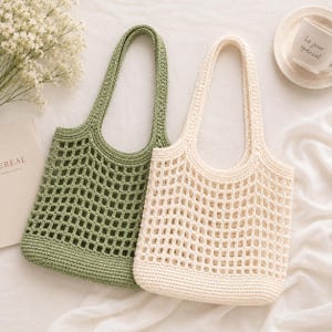 May include: Two crochet tote bags with an open square mesh pattern and solid base. One bag is sage green and the other is off-white. Both bags feature two integrated shoulder straps and a structured bottom section made of dense crochet stitches.