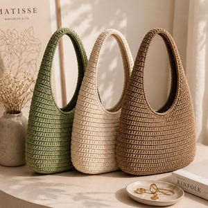 Peut inclure: Trois sacs &agrave; main de style hobo fabriqu&eacute;s en fil crochet&eacute;, dot&eacute;s d'une anse int&eacute;gr&eacute;e unique et d'un motif c&ocirc;tel&eacute; textur&eacute;. Les sacs sont pr&eacute;sent&eacute;s en trois couleurs distinctes : vert sauge, cr&egrave;me et brun clair, dispos&eacute;s c&ocirc;te &agrave; c&ocirc;te.