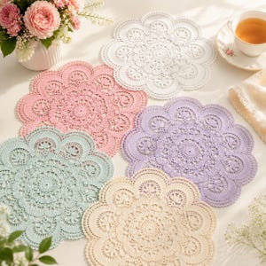 May include: A collection of five round, scalloped-edge lace doilies in white, soft pink, light purple, mint green, and cream. Each doily features an intricate, symmetrical floral and geometric pattern with a central circular motif.