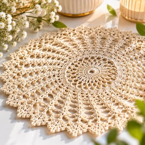 May include: A round, cream-colored crochet doily featuring an intricate, radiating starburst pattern with delicate openwork stitches and a scalloped edge. The textile piece displays a complex, symmetrical design that expands from the center outward.