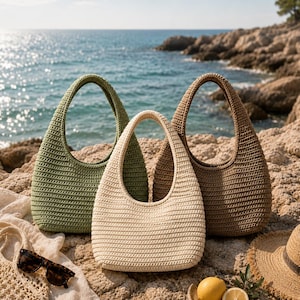 Peut inclure: Trois sacs &agrave; main de style hobo fabriqu&eacute;s en fil crochet&eacute; de couleur vert olive, cr&egrave;me et marron. Chaque sac pr&eacute;sente une anse int&eacute;gr&eacute;e unique et une base arrondie. Les sacs sont dispos&eacute;s ensemble, mettant en valeur leur texture c&ocirc;tel&eacute;e.