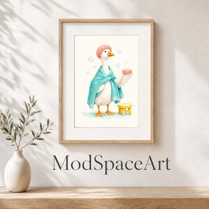 May include: A framed art print featuring a white goose wearing a pink shower cap and a blue towel wrapped around its body. The goose holds a small pink bar of soap in one wing, standing next to a small yellow stool with floating bubbles.