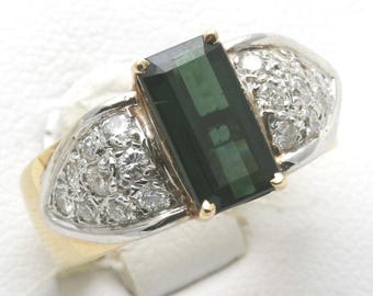 Può includere: Un anello in oro e argento con una grande gemma rettangolare verde scuro al centro. Ai lati della pietra centrale, ci sono gruppi di piccole gemme chiare, creando un design lussuoso ed elegante.