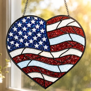 Könnte beinhalten: Herzförmige Glasdekoration mit dem Design der amerikanischen Flagge. Die obere linke Ecke hat einen blauen Hintergrund mit weißen Sternen, während der Rest rote und weiße Streifen zeigt. Es hängt an einer schwarzen Kette.