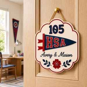 May include: A cream-colored scalloped wall sign hanging by a gold cord. It features the number 105 in dark blue, a navy blue pennant with red HSA lettering, the name Avery & Mason in black script, and a red flower with dark blue leaves below.