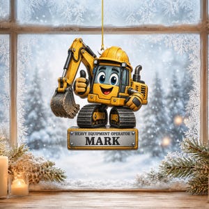 May include: A yellow excavator ornament with a cartoon face, wearing a hard hat, giving a thumbs up. Below the excavator is a rectangular metal-look plaque with the text HEAVY EQUIPMENT OPERATOR and the name MARK in bold black letters.