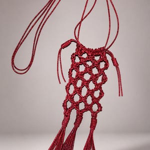 May include: A deep red macrame pouch featuring a shimmering, glittery texture. The body is constructed with an open, knotted lattice pattern, finished at the bottom with three long, thick tassels. It includes a matching thin cord for hanging.