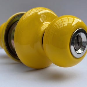 May include: A bright yellow door knob with a keyhole and a shiny finish. The knob is round and has a metallic silver trim around the keyhole. The door knob is a hardware item.