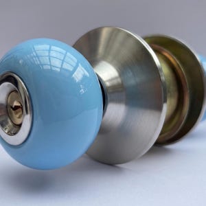 May include: A light blue door knob with a shiny, rounded handle. The knob has a keyhole and is made of metal and ceramic. The door knob is designed for interior doors.