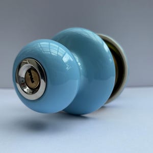 May include: A light blue door knob with a keyhole and a shiny, rounded design. The knob has a metallic base and a glossy finish, suitable for interior doors. The keyhole is centered on the smaller knob.