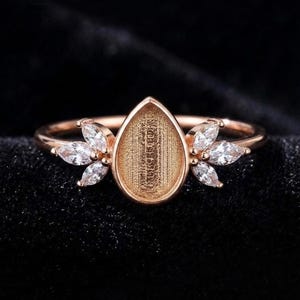Peut inclure: Une bague en or rose dotée d'un sertissage central en forme de poire avec une surface texturée et en creux. Le sertissage est flanqué de chaque côté de trois pierres claires taille marquise disposées en motif de feuille.
