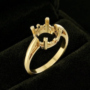 Pode incluir: Um anel de ouro amarelo polido com uma cabeça intrincada e vazada em estilo coroa, projetada para segurar uma pedra preciosa. A banda é lisa e sólida, levando a uma galeria decorativa de estilo filigrana que sustenta as garras centrais.