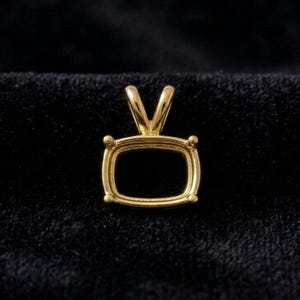 May include: A gold-toned pendant setting featuring a rectangular frame with rounded corners and four prongs at each corner. The piece includes a V-shaped bail at the top for attachment to a chain, showcasing a polished metallic finish throughout.