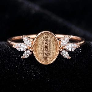 May include: Rose gold ring with an oval setting and marquise-cut white gemstones. The ring has a floral design on each side of the oval setting, adding a delicate and elegant touch to the jewellery.