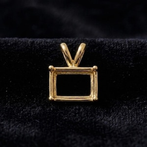 May include: A gold-toned rectangular pendant setting featuring a hollow centre for a gemstone. The piece includes a V-shaped bail at the top for attachment to a chain, with four small prongs at the corners to secure a stone in place.