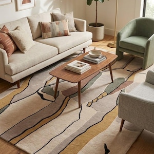 Könnte beinhalten: Ein großer Teppich mit einem abstrakten Muster aus wellenförmigen Linien und organischen Formen in Beige, Senfgelb, Salbeigrün und Schwarz. Der Teppich liegt unter einem hölzernen Couchtisch, einem beigen Sofa, einem salbeigrünen Sessel und einem grauen Stuhl.