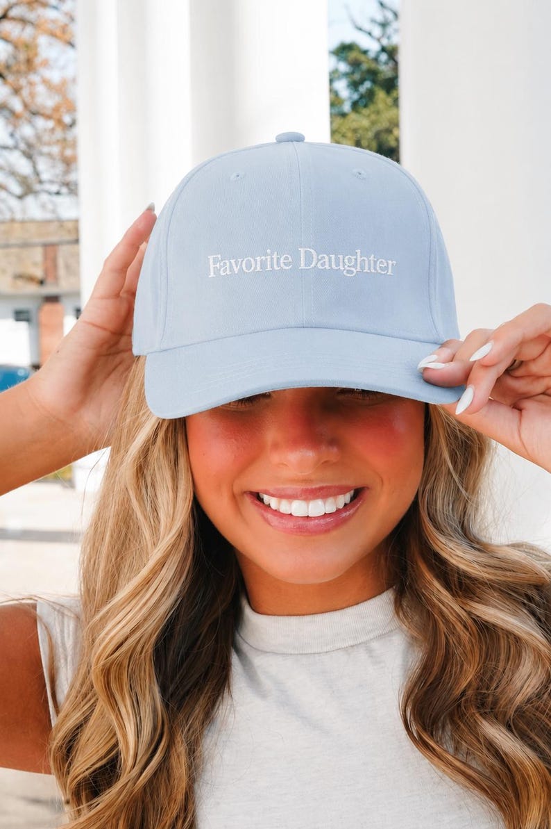 May include: A light blue baseball cap featuring the text Favorite Daughter embroidered in white thread on the front panel. The cap has a structured crown, a curved brim, and a button on top, providing a clean and simple design for casual wear.