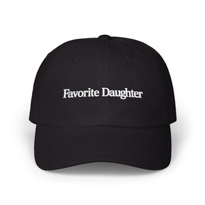 May include: A black baseball cap featuring the text Favorite Daughter embroidered in white thread across the front panel. The cap has a structured crown, a curved brim, and a button at the top center, providing a clean and simple design.