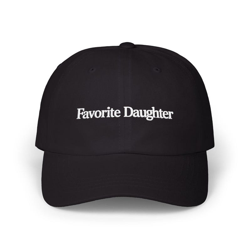 May include: A black baseball cap featuring the text Favorite Daughter embroidered in white thread across the front panel. The cap has a structured crown, a curved brim, and a button at the top center, providing a clean and simple design.