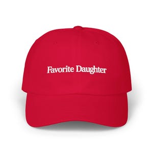 May include: A bright red baseball cap featuring the text Favorite Daughter embroidered in white across the front panel. The cap has a structured crown, a curved brim, and a button at the top center, providing a classic look with bold contrast.