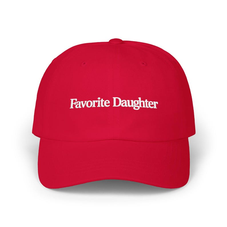 May include: A bright red baseball cap featuring the text Favorite Daughter embroidered in white across the front panel. The cap has a structured crown, a curved brim, and a button at the top center, providing a classic look with bold contrast.