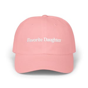 May include: A light pink baseball cap featuring the text Favorite Daughter embroidered in white thread across the front center. The cap has a structured crown, a curved brim, and a button on the top, presenting a clean and simple design.