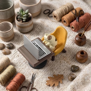 May include: A miniature figurine of a cream and brown cat sitting in a yellow armchair at a small brown desk with a silver laptop. The scene includes ceramic pots, spools of colored twine, wooden inkwells with a quill, scissors, and stones.