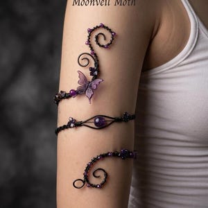 May include: Black wire arm jewelry with purple beads and a butterfly accent. The jewelry is designed in a spiral and curved shape. The text "Moonveil Moth" is visible in the upper left corner.