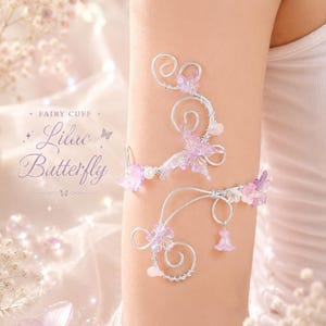 May include: Delicate silver-toned arm cuffs adorned with lilac butterfly and floral accents. The cuffs feature swirling wire designs and small, translucent beads. Text on the image reads "FAIRY CUFF" and "Lilac Butterfly".