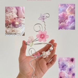 May include: A silver-toned wire floral bracelet with pink and clear flower accents. The bracelet is adorned with small pearls and the text "Blush Blossom" in pink.
