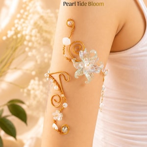 May include: A gold-toned arm cuff with a floral design and the text "Pearl Tide Bloom." The cuff features a delicate arrangement of pearls, white flower accents, and a large, translucent flower. The design is intricate and elegant.