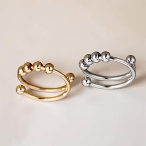 May include: Two rings, one gold-toned and one silver-toned, are displayed. Each ring features a double band design with small, spherical beads. The gold ring has a warm, shiny finish, while the silver ring has a polished, reflective surface.