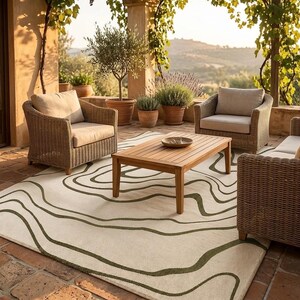May include: A rectangular area rug featuring a cream-coloured base with dark green, flowing, organic topographic-style contour lines. The rug is positioned on a terracotta tiled floor beneath a wooden coffee table and wicker patio furniture.