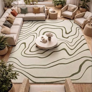 May include: A large rectangular area rug featuring an off-white base colour with dark olive green wavy, organic lines that mimic topographic map contours. The rug is positioned centrally in a room, covering the floor space beneath a coffee table.