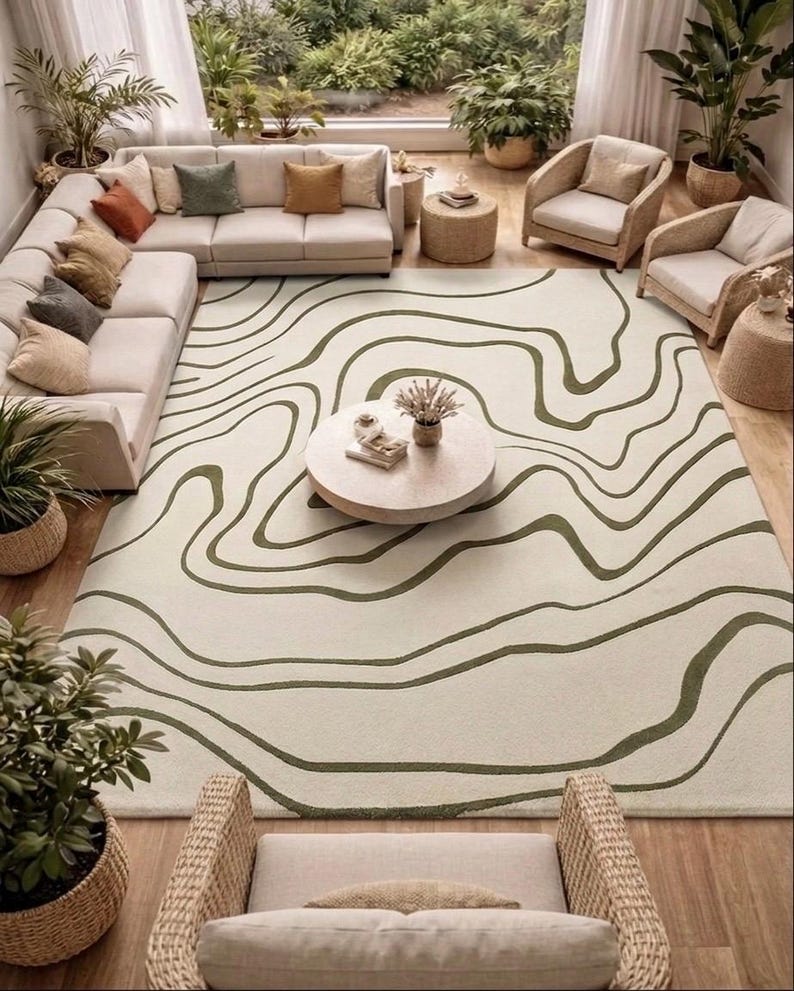May include: A large rectangular area rug featuring an off-white base colour with dark olive green wavy, organic lines that mimic topographic map contours. The rug is positioned centrally in a room, covering the floor space beneath a coffee table.
