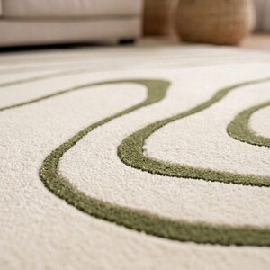 May include: A plush area rug featuring a cream-coloured base with raised, textured olive green lines that form organic, flowing curves across the surface. The rug has a soft, tufted pile construction with a distinct contrast between the colours.