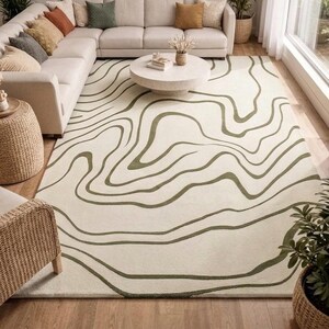 May include: A rectangular area rug featuring a cream-coloured base with dark olive green wavy, topographical-style lines that flow across the surface. The rug has a low-pile texture and covers a large portion of the floor space in the room.