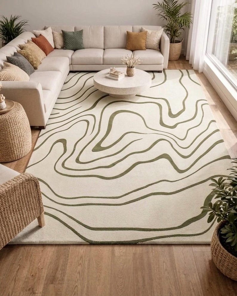 May include: A rectangular area rug featuring a cream-coloured base with dark olive green wavy, topographical-style lines that flow across the surface. The rug has a low-pile texture and covers a large portion of the floor space in the room.