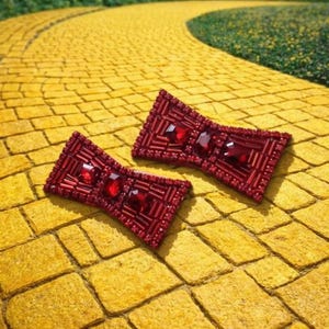 May include: Two bow-shaped accessories embellished with deep red beads and faceted red crystals. The bows feature a rectangular structure with a dense, textured surface created by rows of small beads and larger, prominent central red stones.