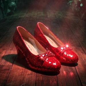 Könnte beinhalten: Ein Paar funkelnde, rote Pailletten-Schuhe mit Schleifendetail. Die Schuhe haben einen kleinen Absatz und werden auf einer Holzoberfläche präsentiert. Die Schuhe sind von der Marke "Morgen Shoe Co.".