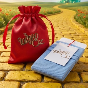 May include: A bright red drawstring pouch featuring The Wizard of Oz logo in gold lettering, paired with a folded pair of light blue ribbed socks that include a white tag with The Wizard of Oz logo attached by a thin red string.