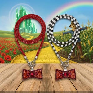 May include: Two lanyards with bow-shaped charms. One lanyard is solid red with sparkling crystals, and the other features a black and white checkered pattern. Both charms are red with rectangular red stones and metallic accents.