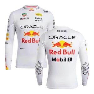 Może przedstawiać: Biała koszulka z długim rękawem z logo Red Bull, przedstawiająca dwa czerwone byki i napis "Red Bull" w kolorze czerwonym. Koszulka wyświetla również logo Oracle i Mobil 1. Dodatkowe logo i tekst są nadrukowane na rękawach.