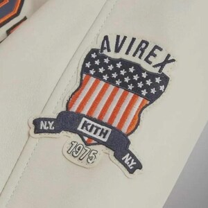 Puede incluir: Una chaqueta de cuero blanca con un parche bordado. El parche muestra el texto AVIREX, KITH, 1975 y N.Y. Incluye un gr&aacute;fico en forma de escudo con un campo azul de estrellas blancas sobre rayas verticales rojas y blancas, bordeado en azul marino.