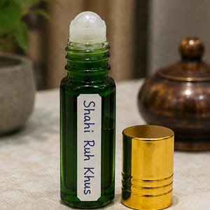 May include: A green glass roll-on bottle with a white label featuring the text Shahi Ruh Khus in blue ink. The bottle has a clear plastic roller ball top and is accompanied by a separate, cylindrical, metallic gold screw-on cap.