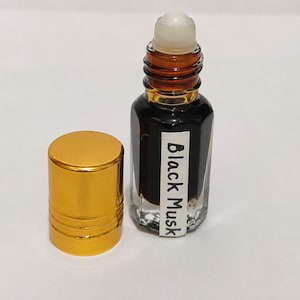 May include: A small glass roll-on bottle filled with dark liquid, featuring a white label with the text Black Musk printed in black. The bottle has a clear roller ball top and is accompanied by a separate, shiny gold-colored cylindrical cap.