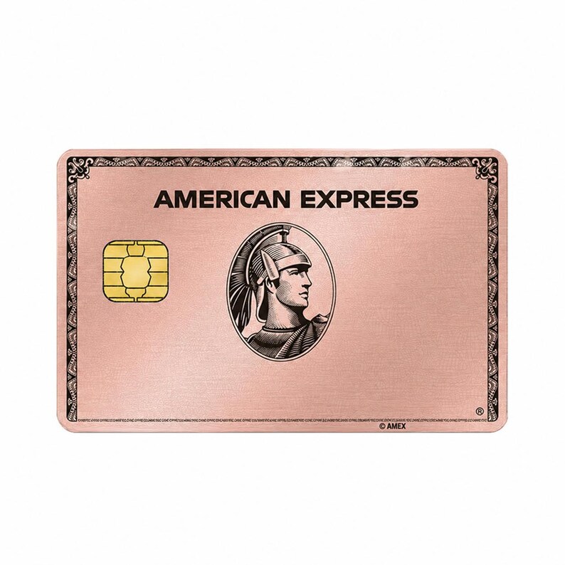 May include: A rose gold-colored American Express credit card featuring a brushed metal finish. The card displays the text AMERICAN EXPRESS at the top, a gold EMV chip on the left, and a central oval emblem depicting a Roman centurion in profile.