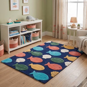 May include: A rectangular navy blue rug with colorful fish and seashell designs. The fish are in shades of blue, green, yellow, and orange, and the seashells are white. The rug is placed on a wooden floor.